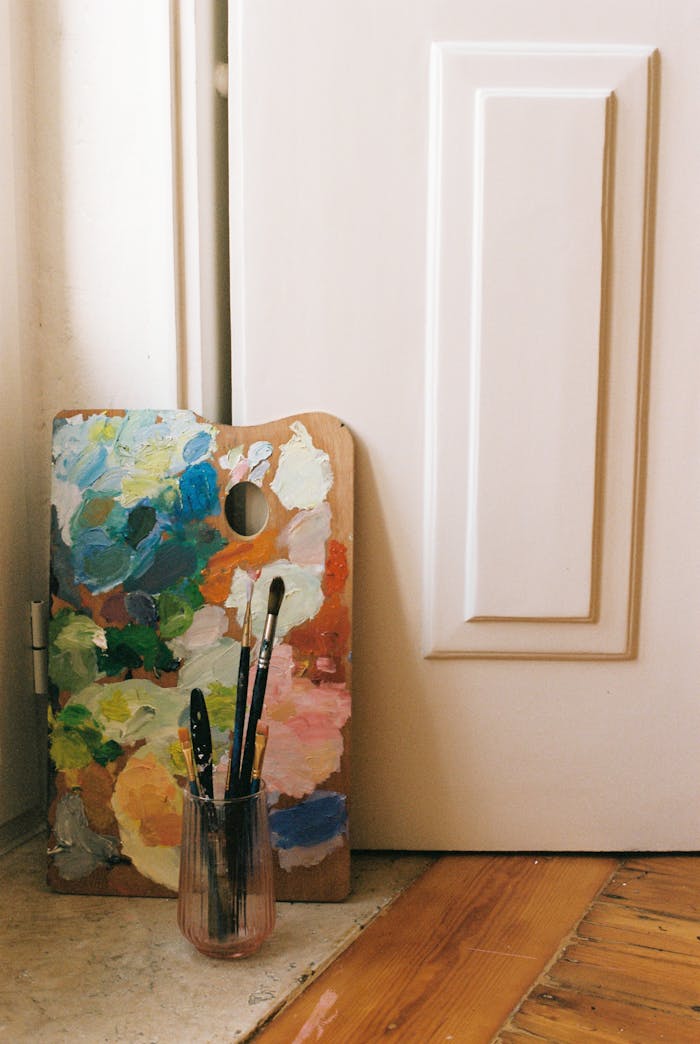 Vibrant artist's palette with brushes leaning against a wooden door, showcasing creativity.