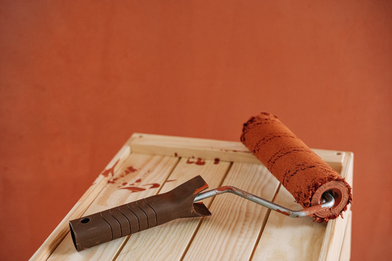 A paint roller with rustic brown paint on a wooden surface against an earthy wall.